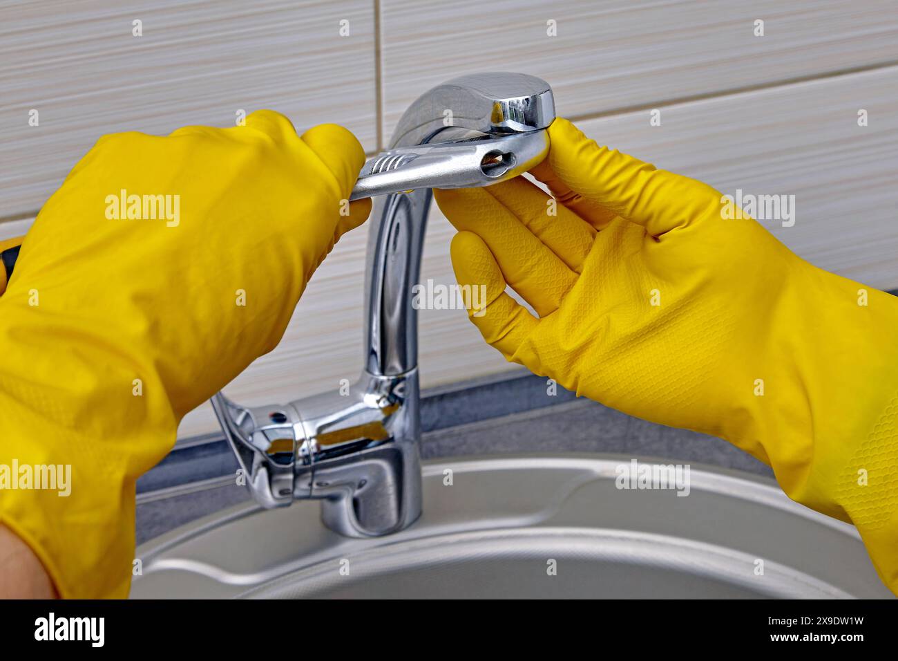 Kitchen faucet repair. A worker in yellow rubber gloves uses an adjustable wrench to unscrew the aerator Stock Photo