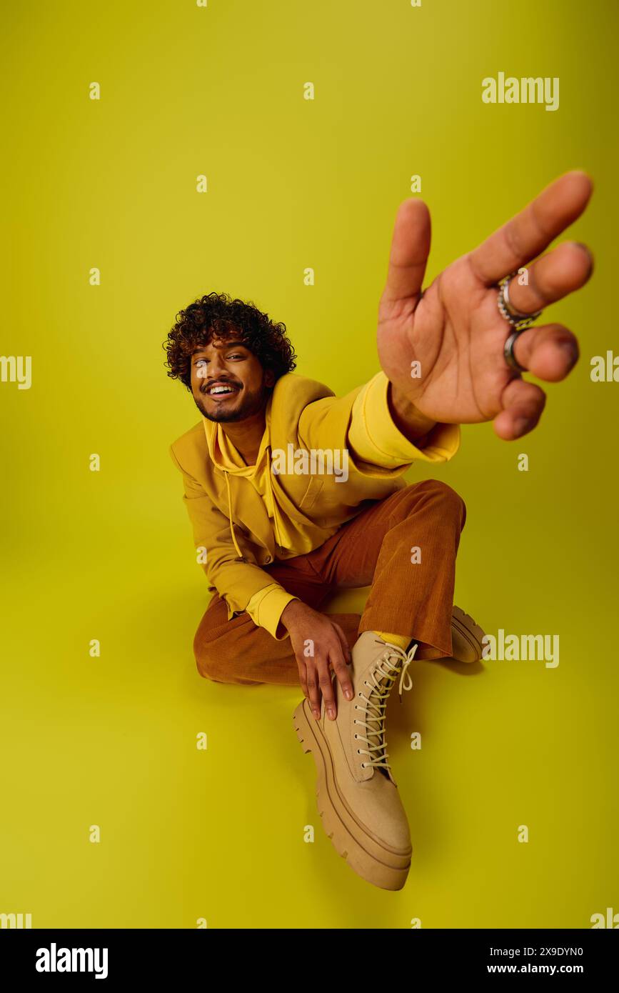 A young Indian man, dressed in vibrant attire, sits on the ground with ...