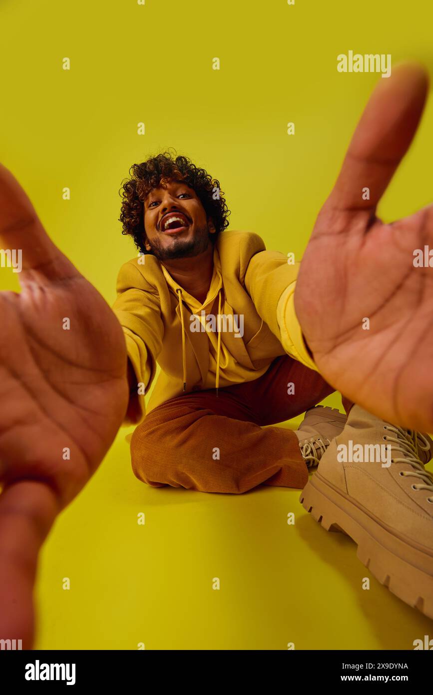 A man in a vibrant outfit sitting on the ground with his hands raised in the air. Stock Photo