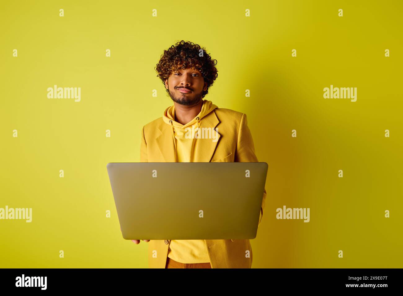 Handsome Indian man in yellow suit poses with laptop. Stock Photo