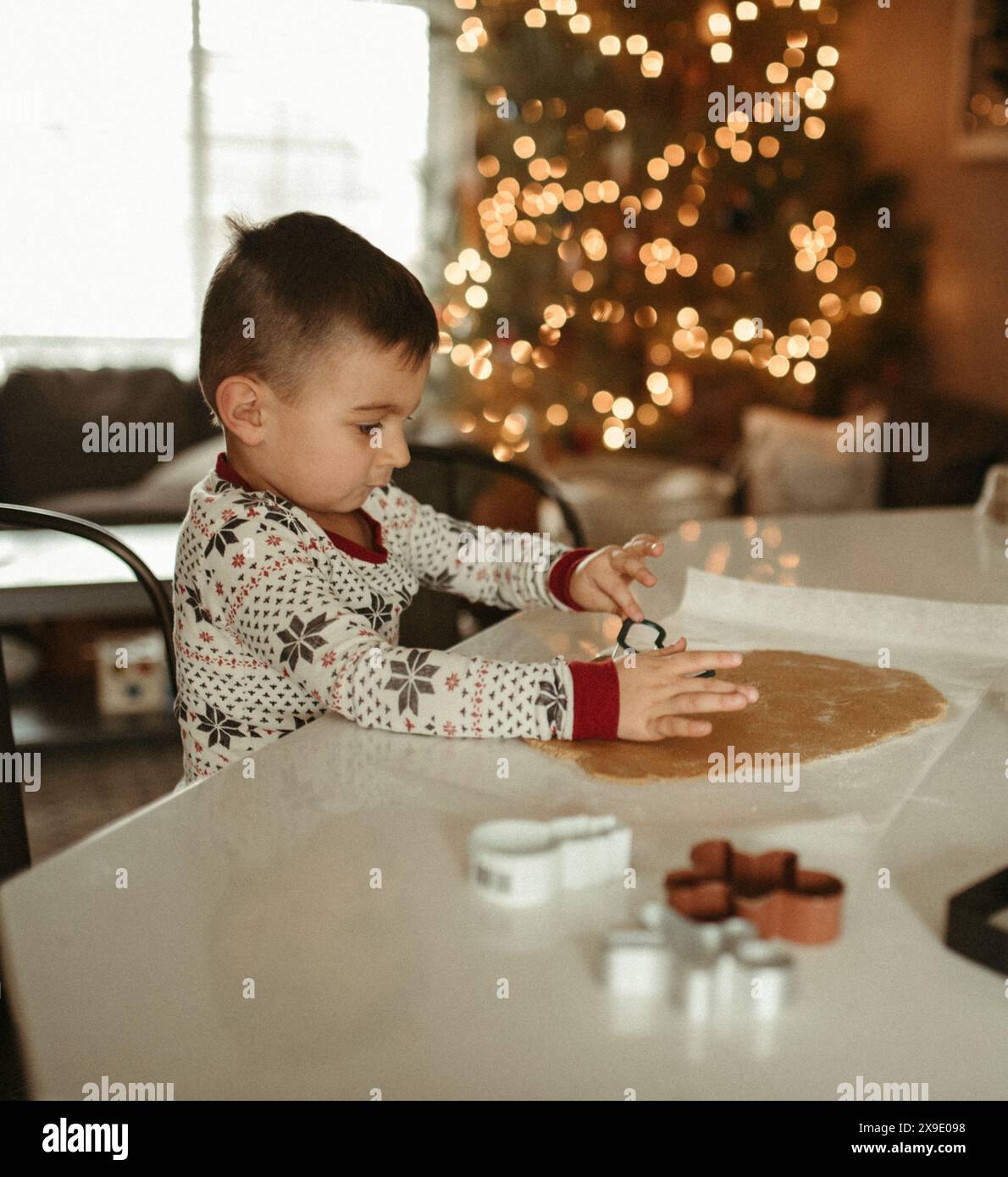 Child in pajamas making holiday cookies in a festive kitchen Stock Photo