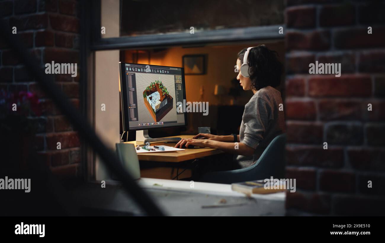 Female Video Game Designer Works on a New 3D Level on Her Personal Computer. Focused Woman Creating Metaverse and Design Video Game. Shot Into the Apartment Window Late at Night. Stock Photo