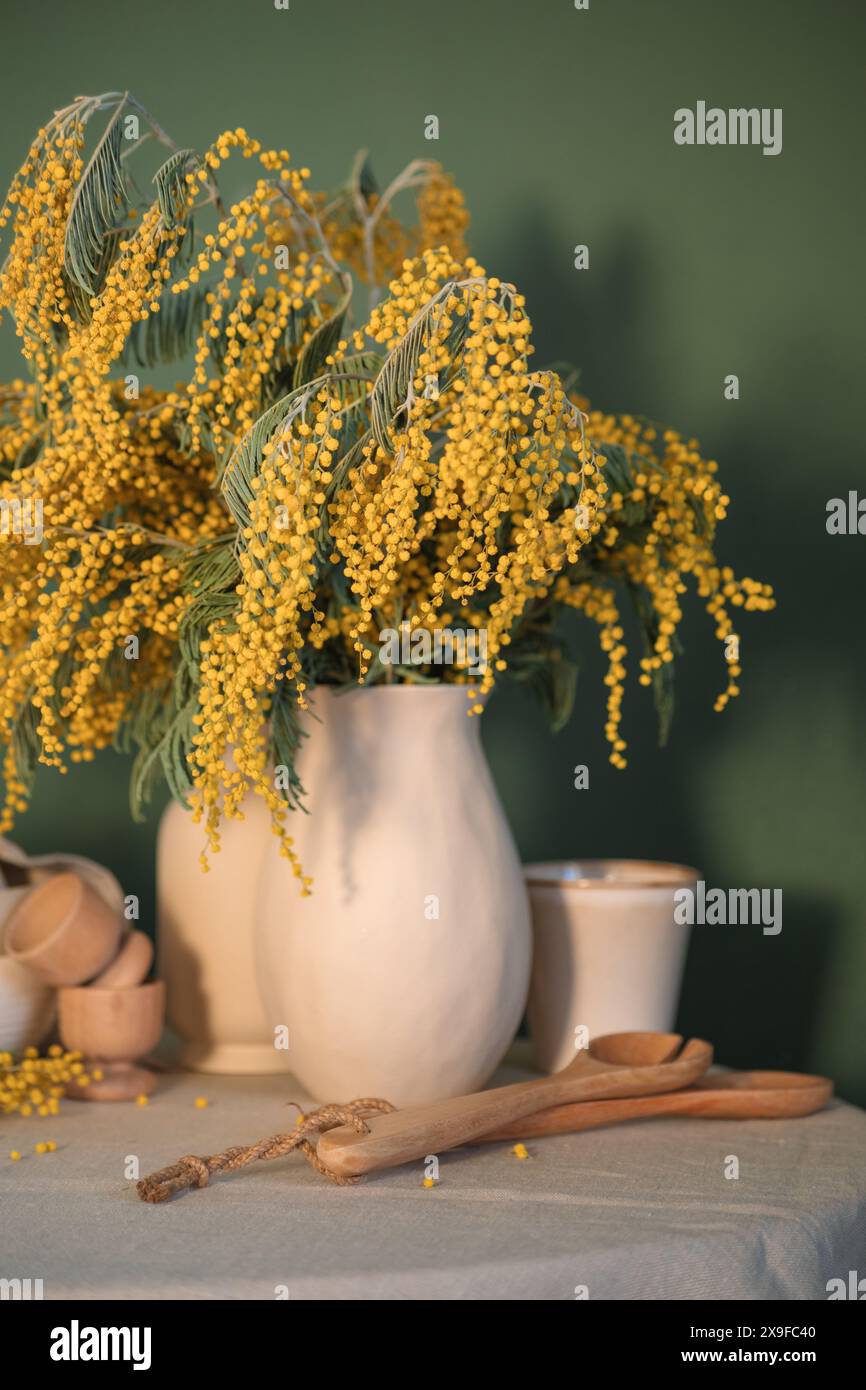 Vase of mimosa flowers on a table with wooden spoons and egg cups Stock Photo