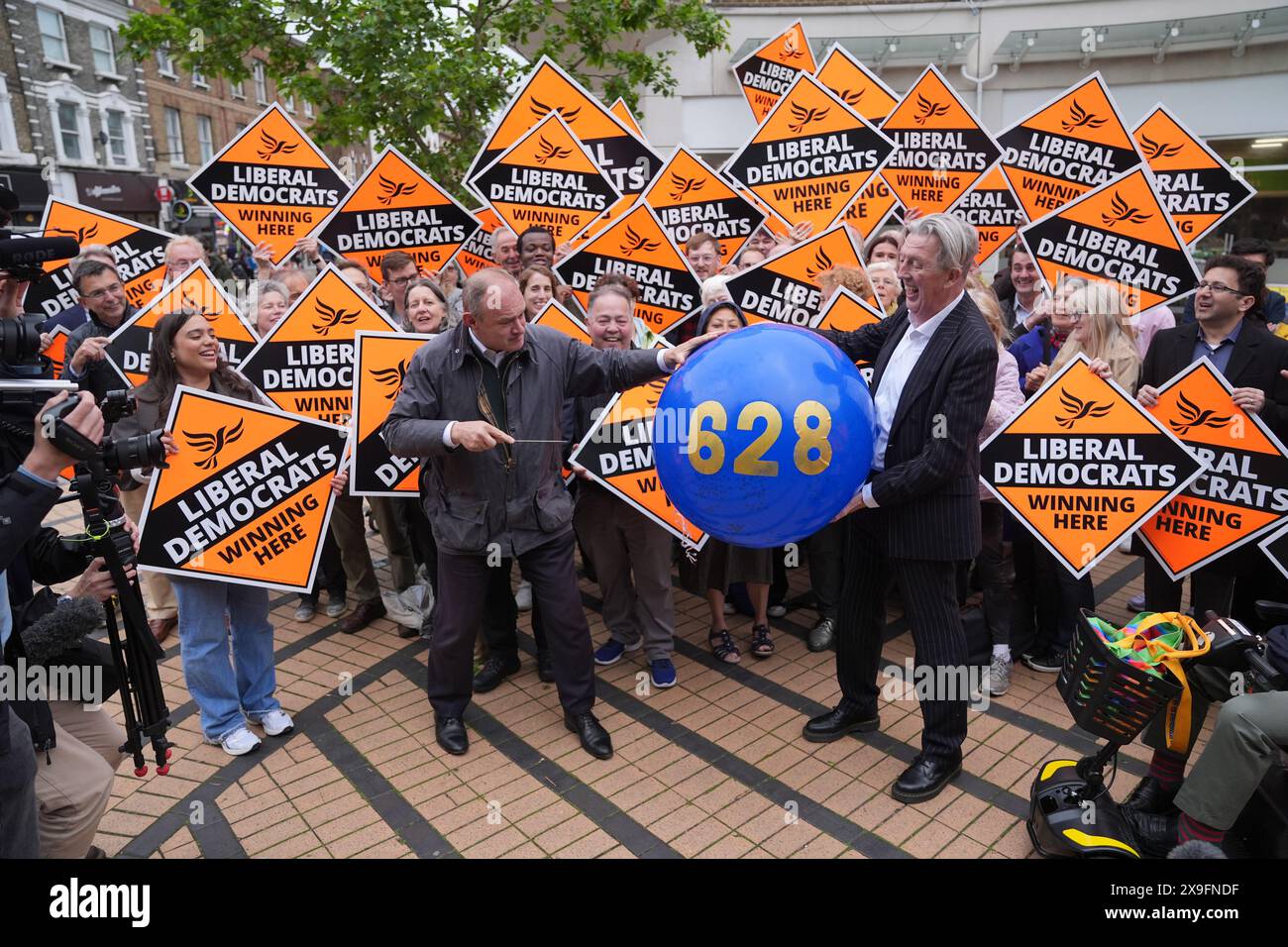 Liberal Democrats leader Sir Ed Davey pops a balloon with Paul Kohler, Wimbledon's parliamentary candidate, outside Morrison's supermarket in Wimbledon, while on the General Election campaign trail. The figure on the balloon represents the amount of votes the Liberal Democrat party lost by in the previous General Election. Picture date: Friday May 31, 2024. Stock Photo