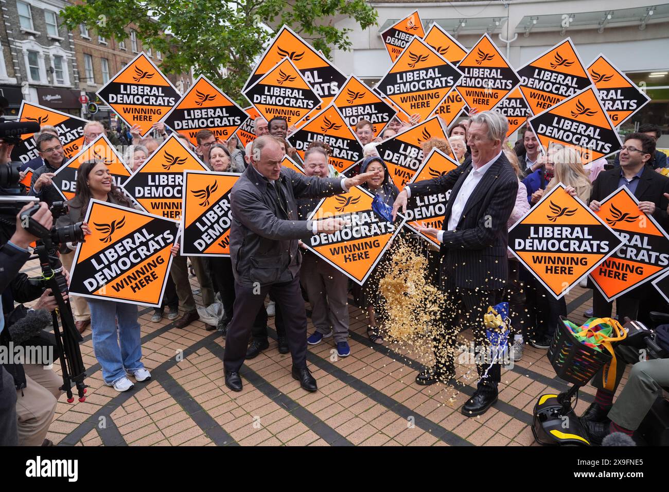 Liberal Democrats leader Sir Ed Davey pops a balloon standing next to Paul Kohler, the Wimbledon parliamentary candidate, outside Morrison's supermarket in Wimbledon, while on the General Election campaign trail. Picture date: Friday May 31, 2024. Stock Photo