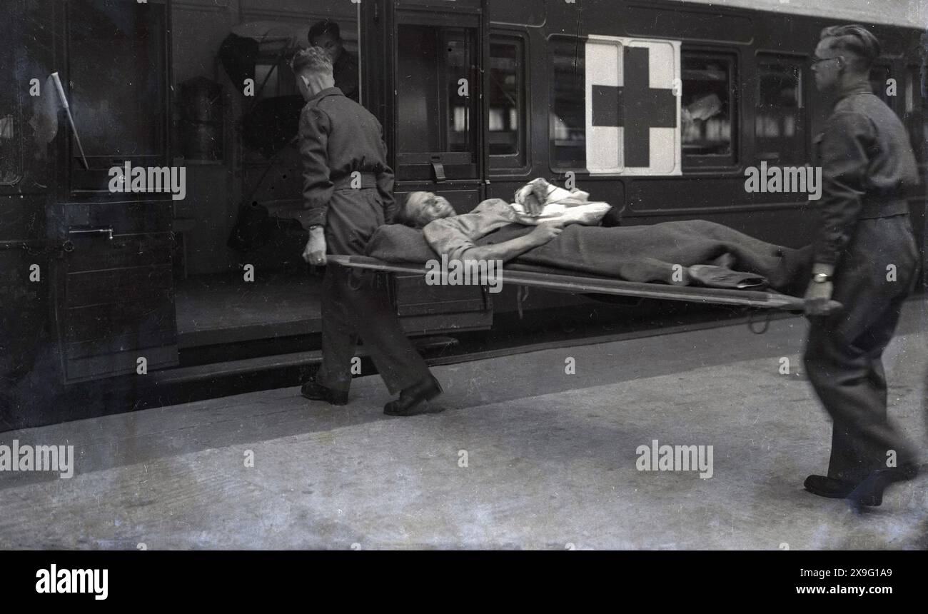 1940, historical, WW2, on a railway platform, two Briitsh soliders carring an injured solider lying on a stretcher onto a train carriage of the red cross, Southampton, England, UK. Known as ambulance trains, they were used to transfer wounded soldiers to military hospitals around the UK for treatment and recuperation. Stock Photo