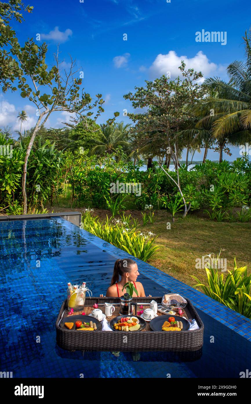 Young happy woman with a floating breakfast in the pool in the The residence luxury resort, Bintan island, Riau islands, Indonesia Stock Photo
