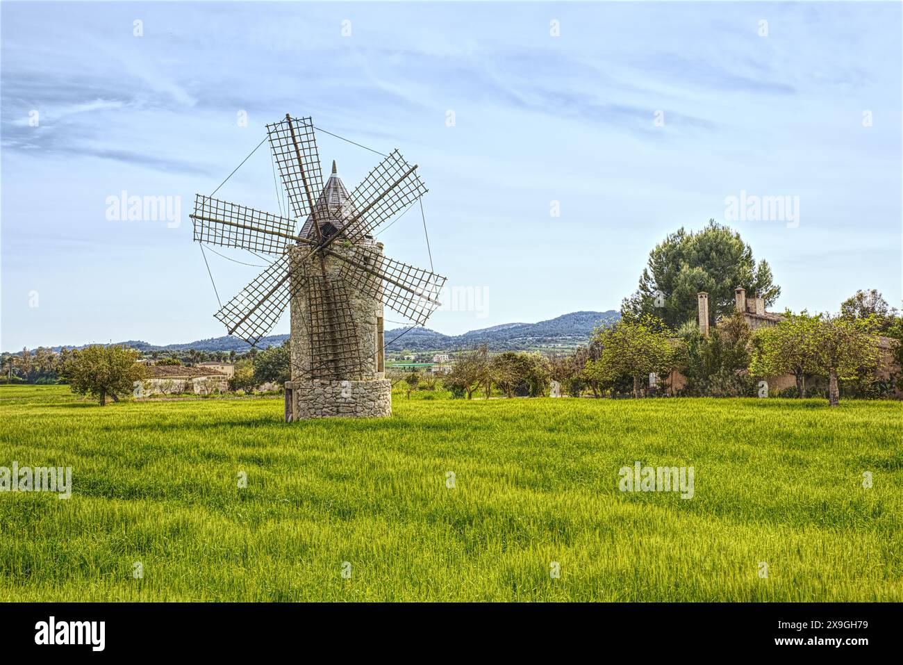 Ancient windmill on green meadow with blue sky and hill at background, Mallorca. Famous tourist attractions in Mallorca - over 5000 windmills all over Stock Photo