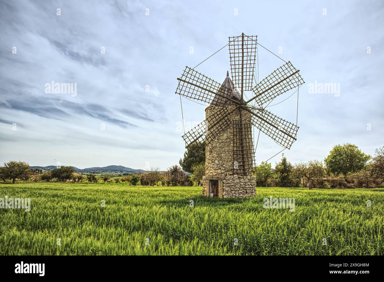 Ancient windmill on green meadow with blue sky and hill at background, Mallorca. Famous tourist attractions in Mallorca - over 5000 windmills all over Stock Photo