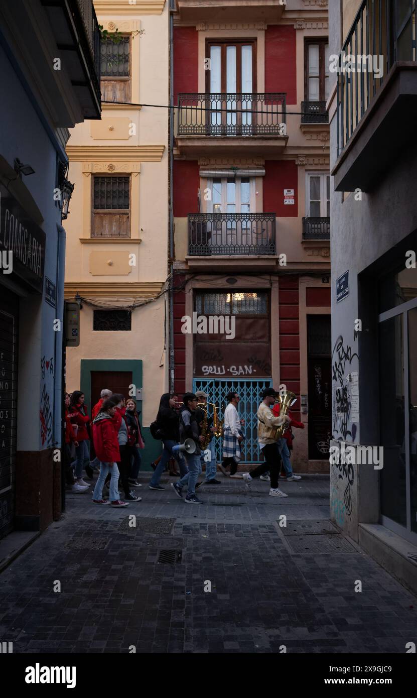 Group in red jackets walks through a narrow, graffiti-lined alley in Valencia, amidst the historic architecture, during the las fallas festivities. Stock Photo