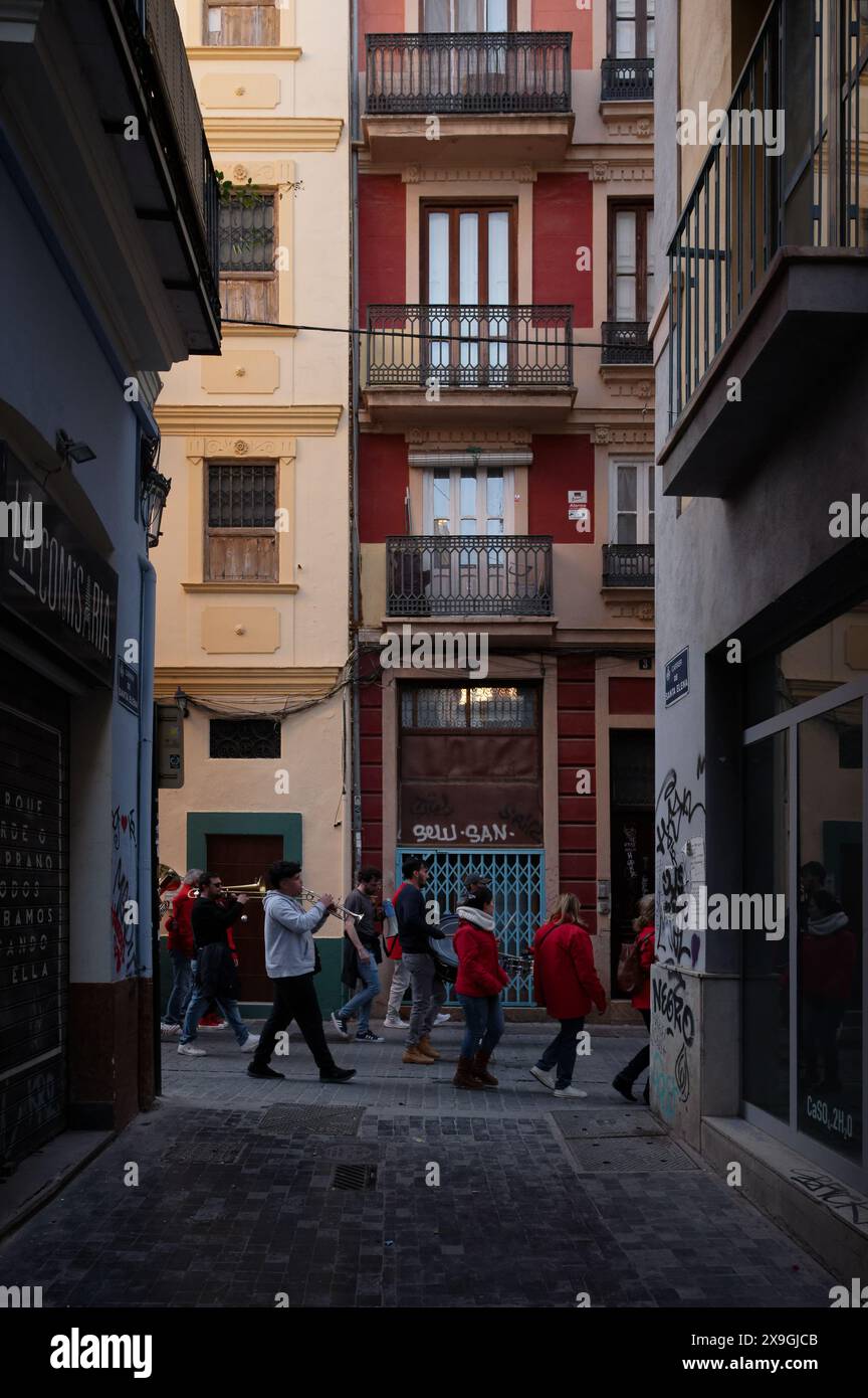 Group in red jackets walks through a narrow, graffiti-lined alley in Valencia, amidst the historic architecture, during the las fallas festivities. Stock Photo