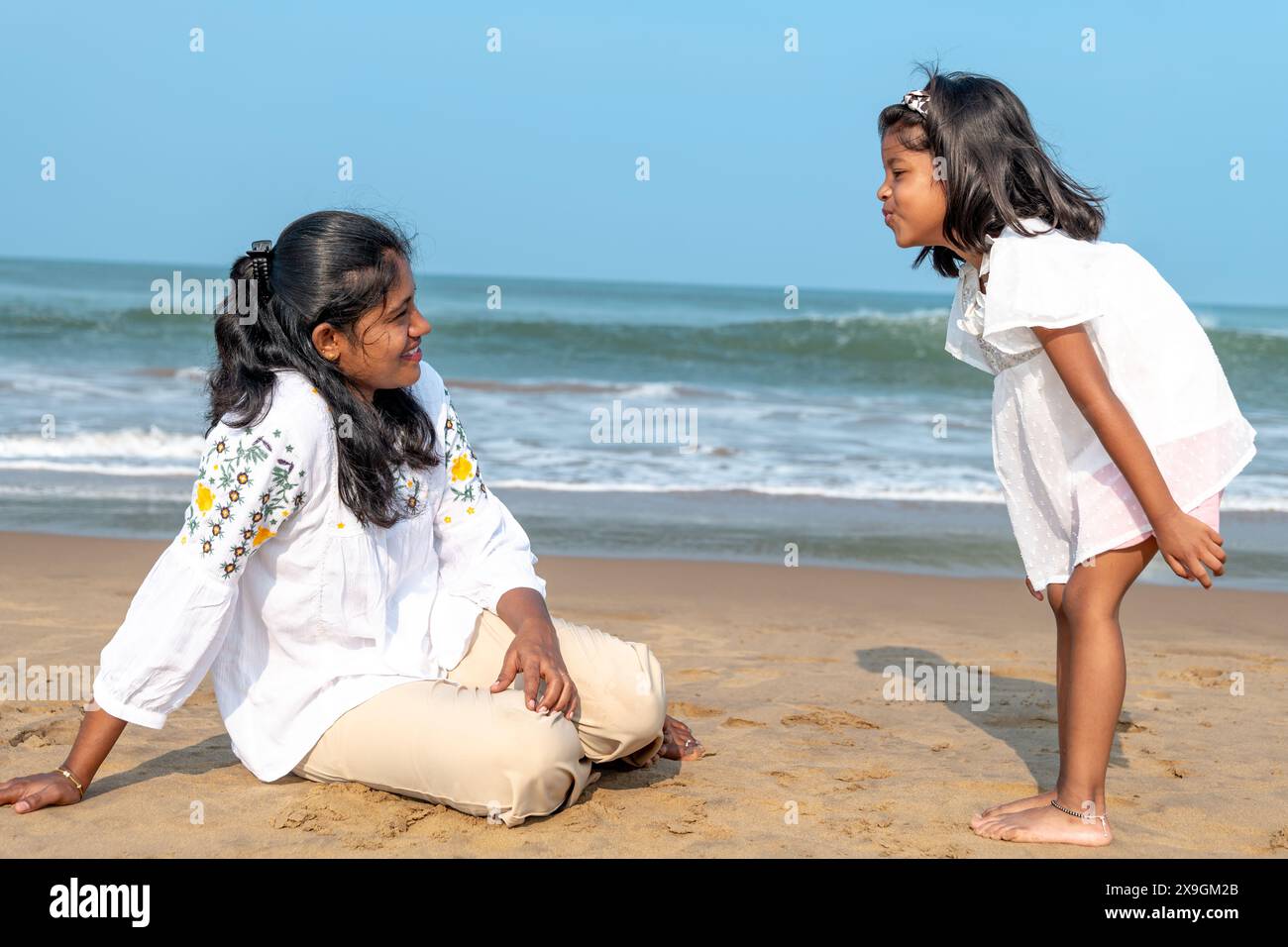 A tranquil day at the beach as a mother watches her daughter play by the ocean. Stock Photo