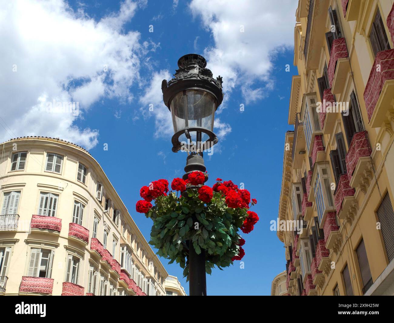 Wrought iron street lamp with red flowers against a clear blue sky and surrounding buildings, the historic fortress of Malaga on the Mediterranean Stock Photo