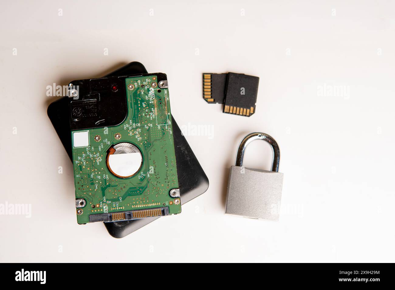 A closed padlock next to two hard disks, in the background a computer keyboard on a white background. Stock Photo