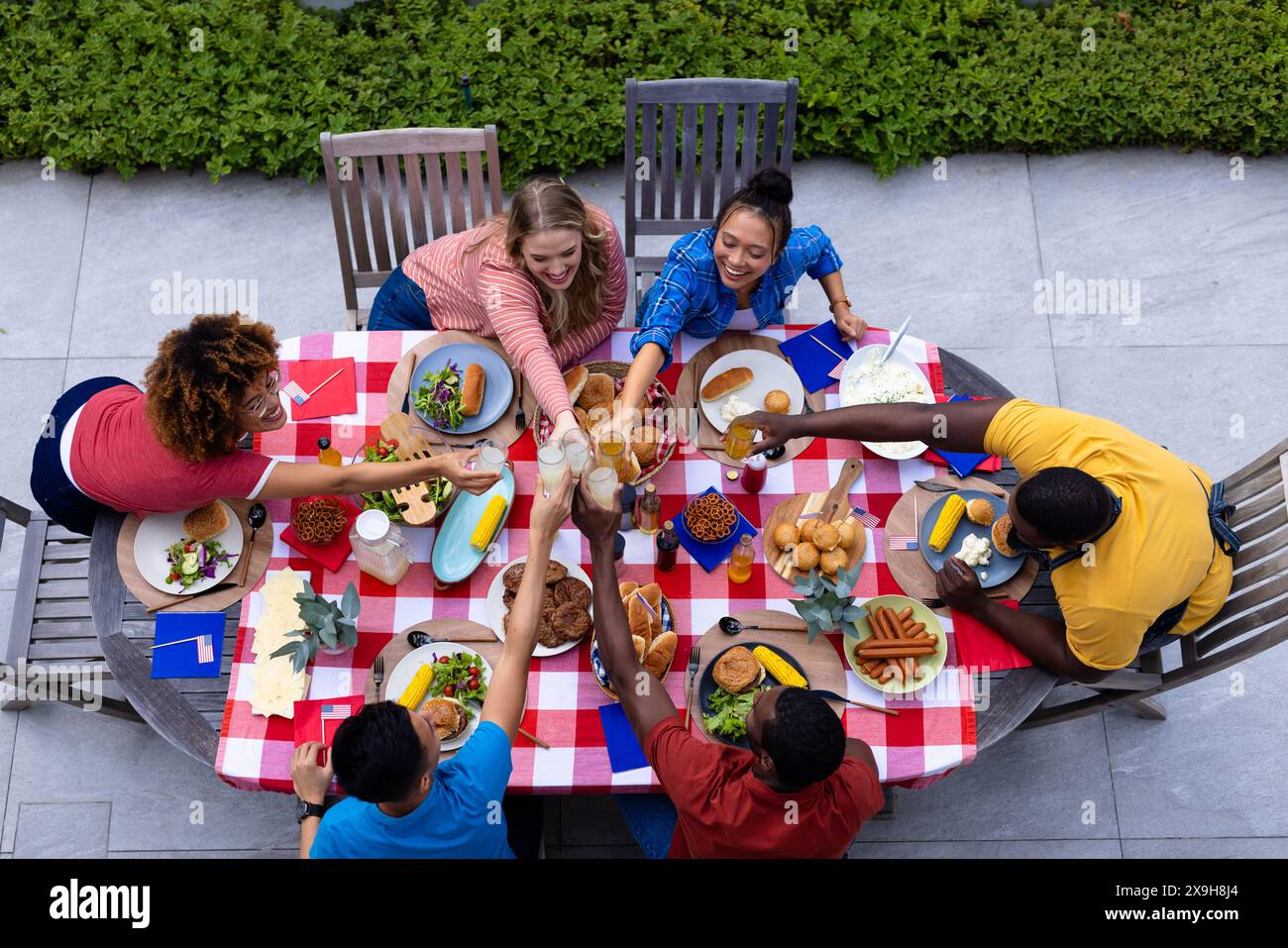 Happy diverse group of friends cheering with drinks and having dinner at balcony with flags of usa Stock Photo