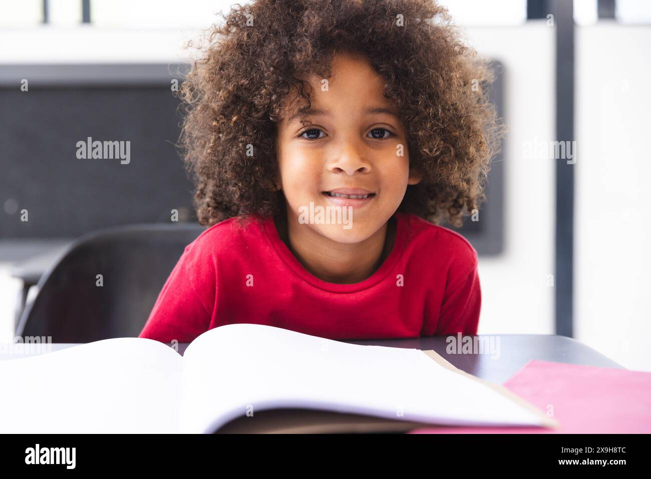 In school, in classroom, biracial young boy leaning on a desk, looking ...