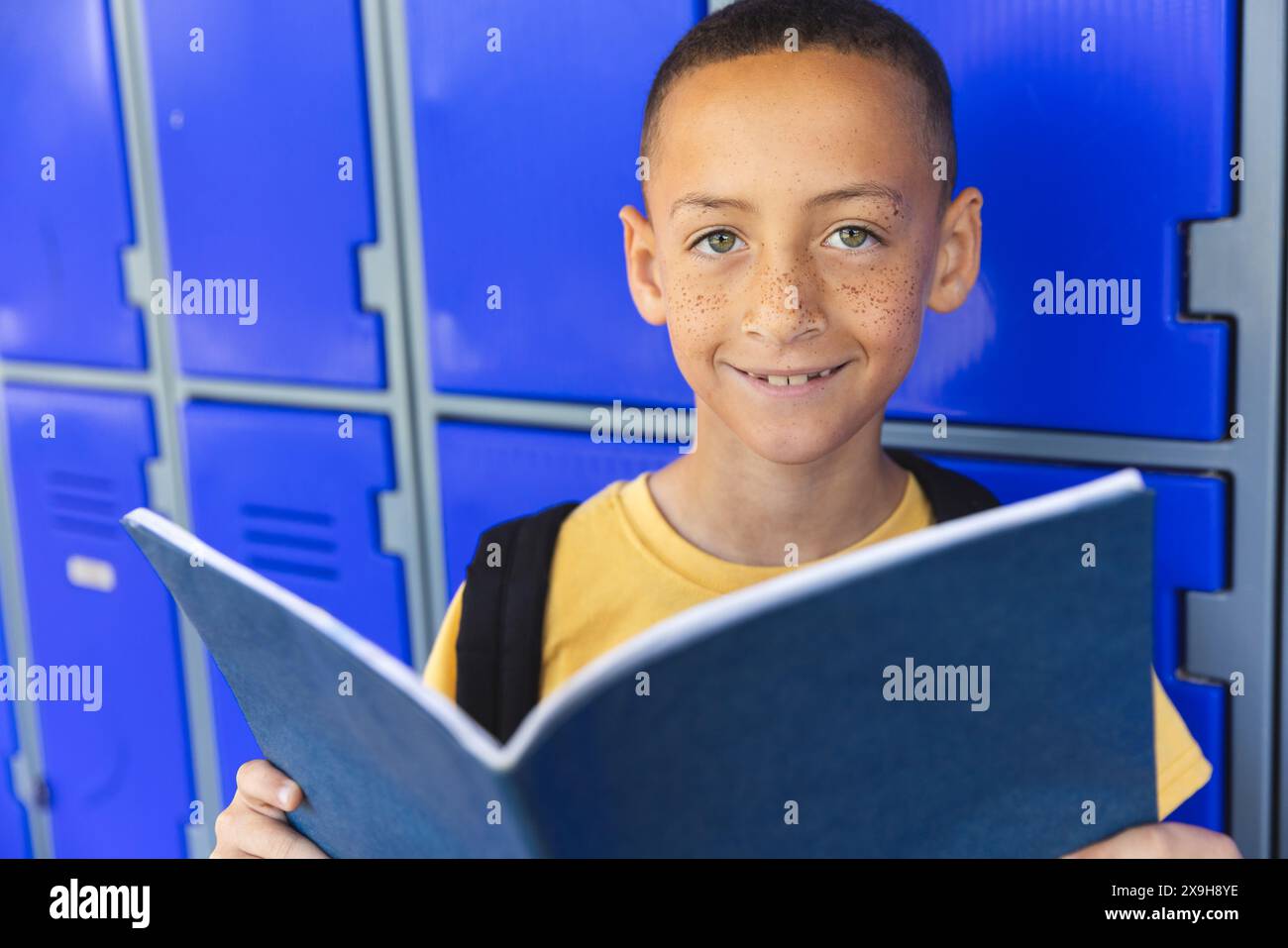 Biracial boy smiles holding a book in school Stock Photo