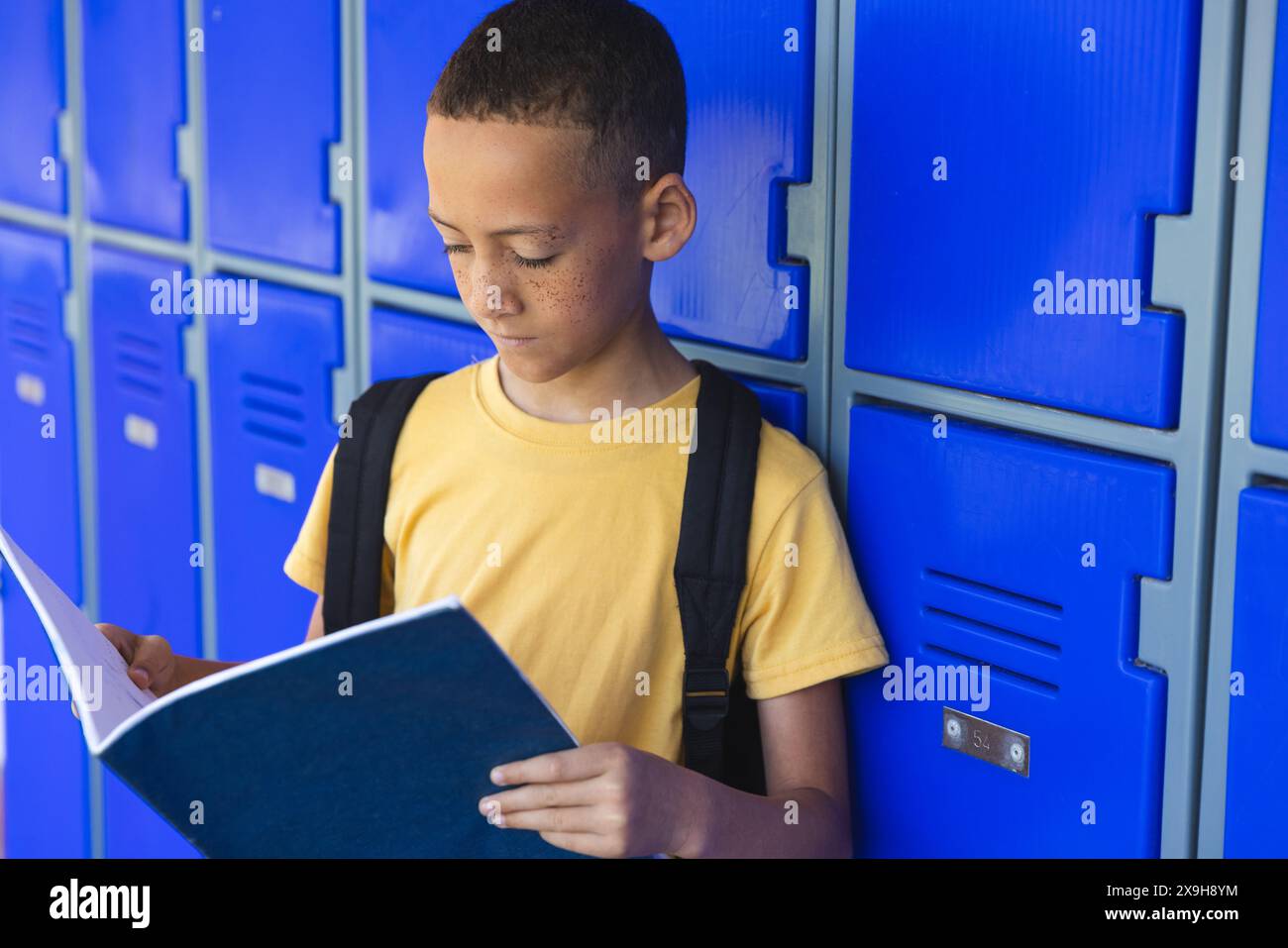 Biracial boy reads a book by his school locker Stock Photo - Alamy