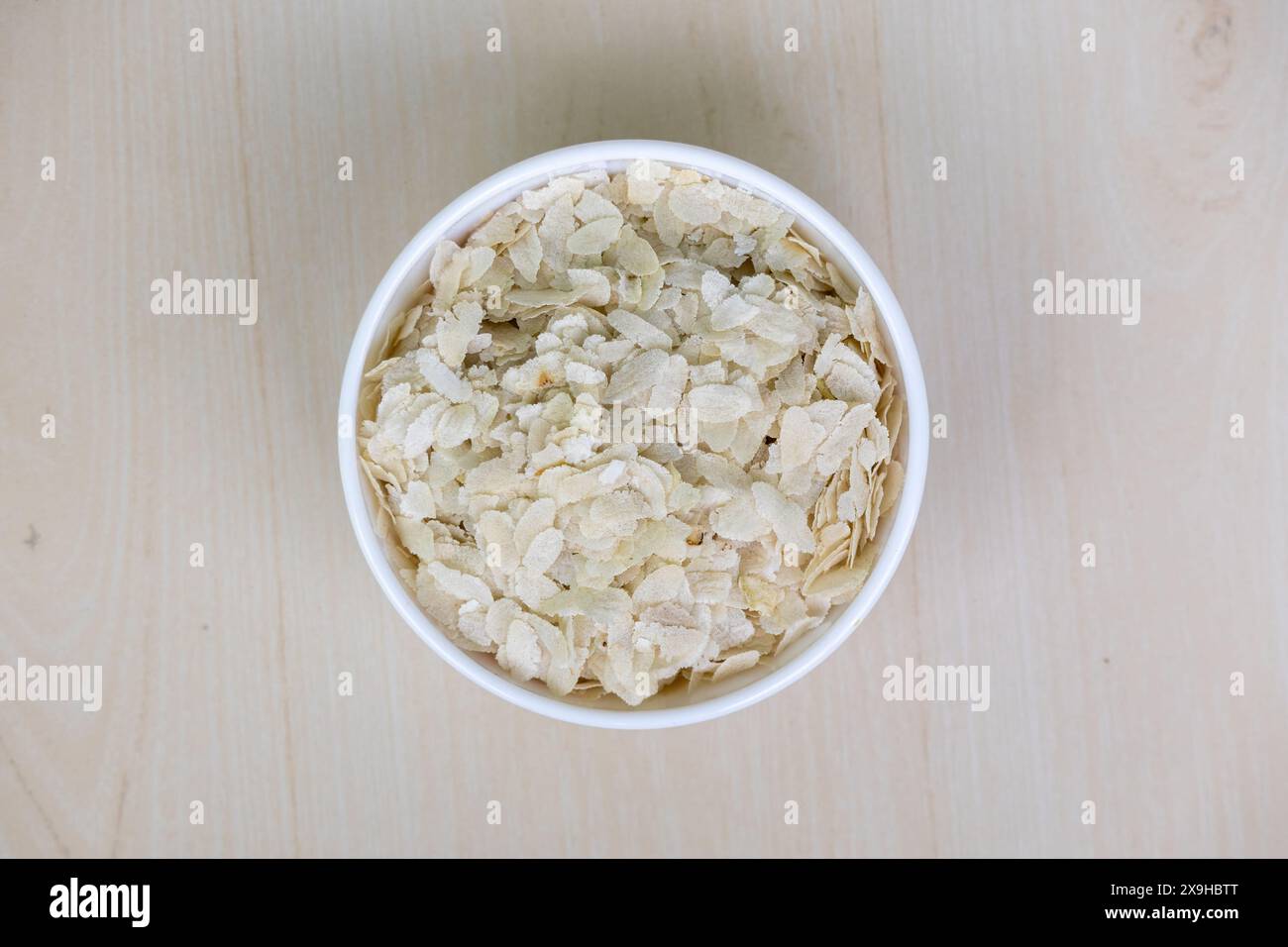 Flattened rice or Chira on a white bowl on a wooden background. It is also known as pohe, aval, pauwa, sira, chivda, or avalakki. Stock Photo