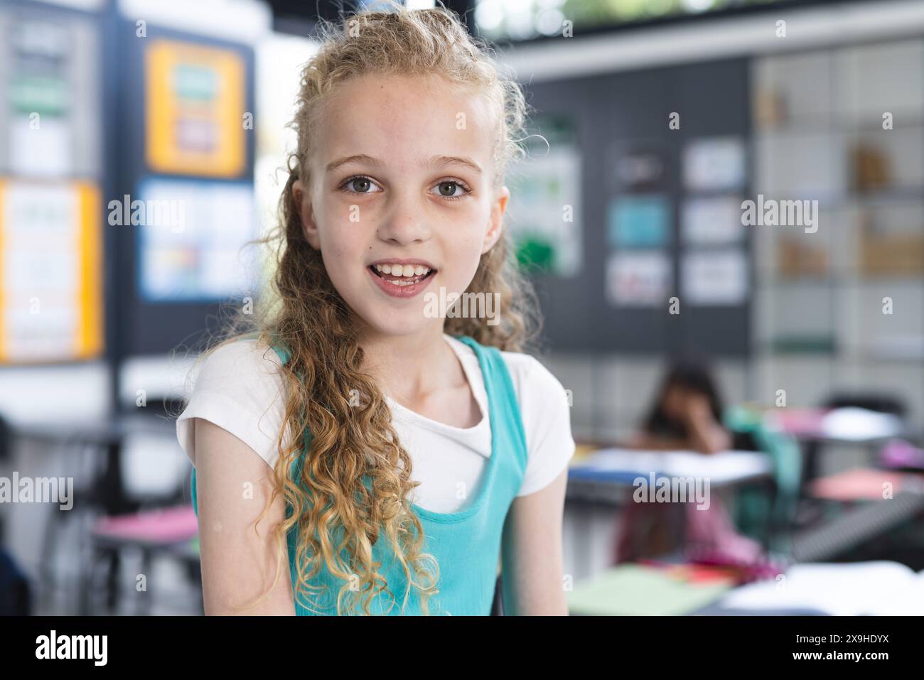 Caucasian girl with curly blonde hair stands in a school classroom Stock Photo