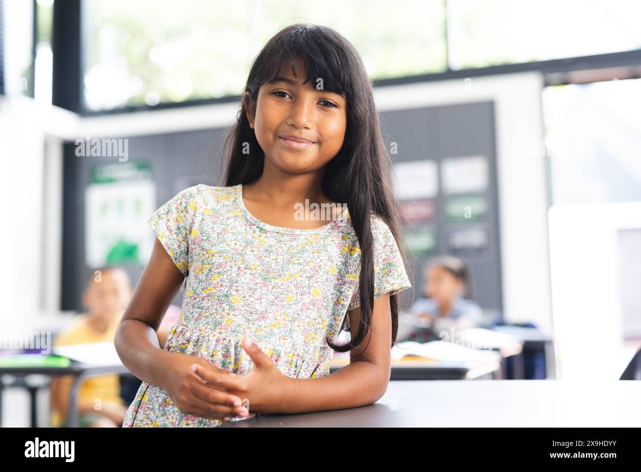 Biracial girl with long brown hair stands smiling in a school classroom Stock Photo