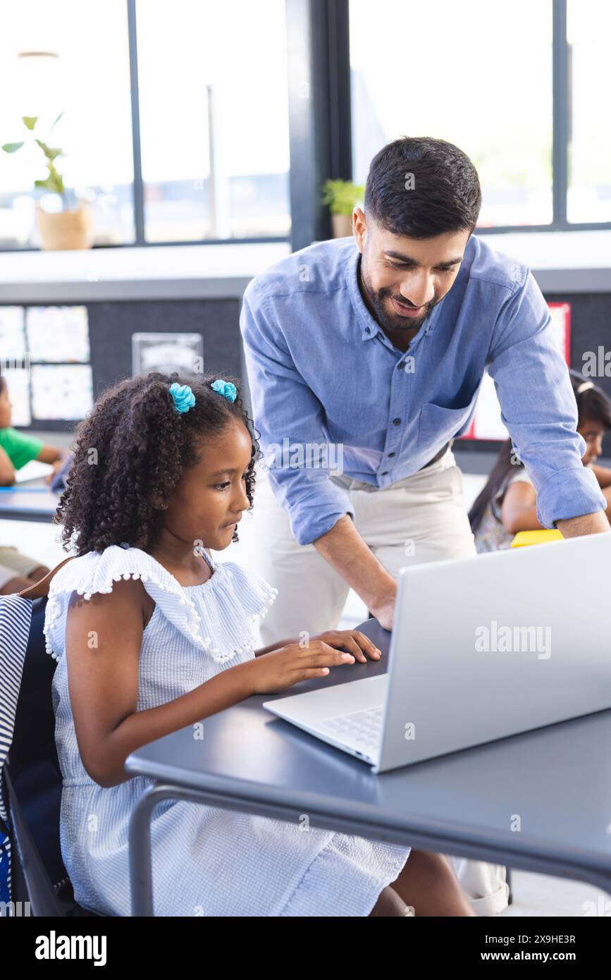 A young Asian male teacher helps biracial girl with her computer work Stock Photo