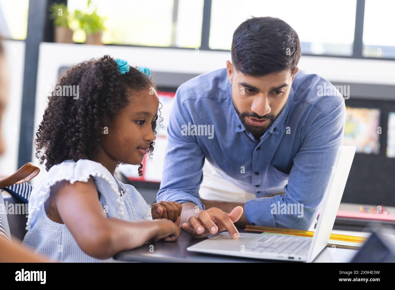 In school, in classroom, Asian male teacher is showing laptop to a young biracial female student Stock Photo