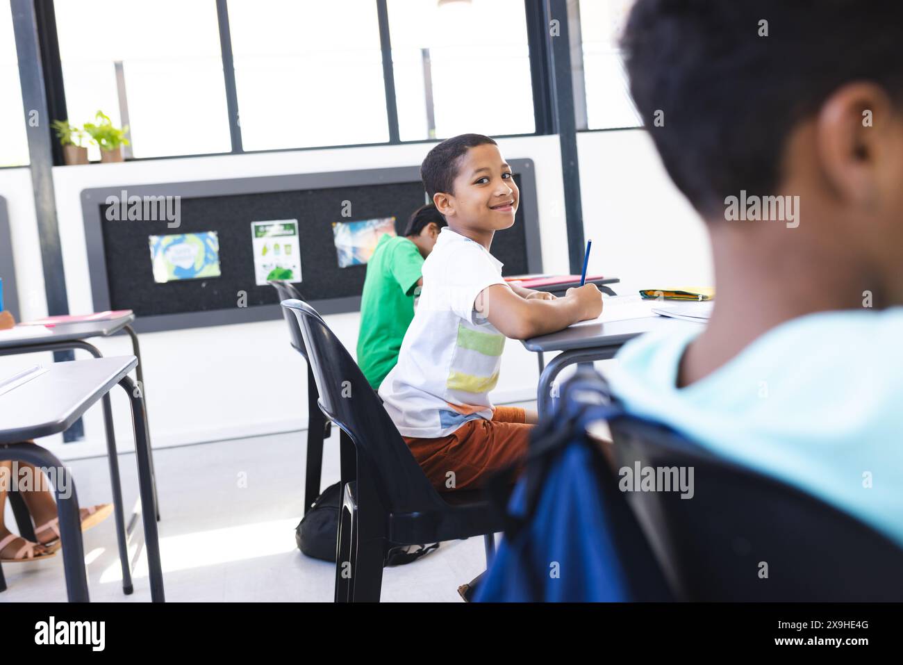 Biracial boy smiles, looks back at classmate in school classroom Stock ...