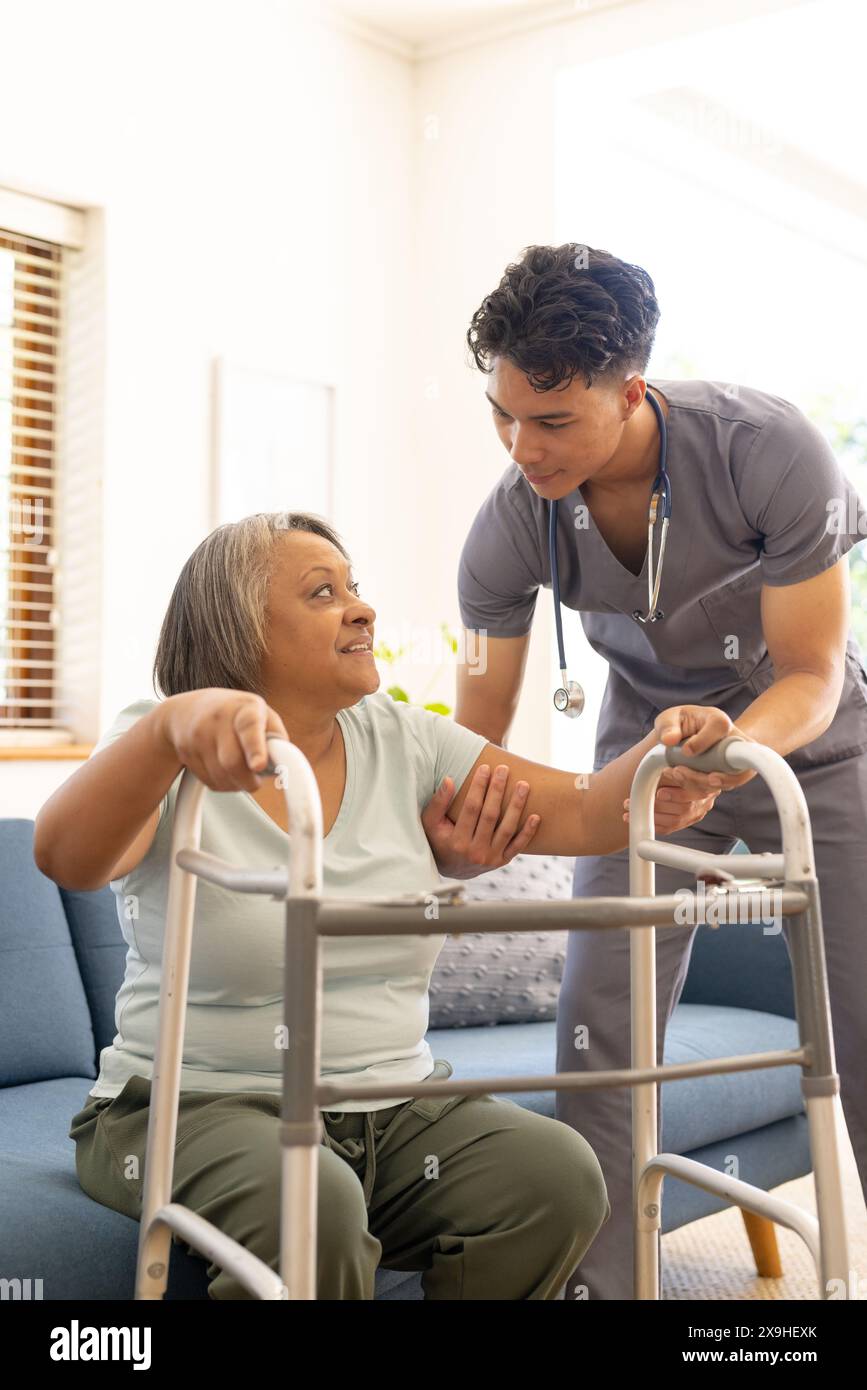 Unalt At home, biracial male nurse helps senior female patient with a walker ...