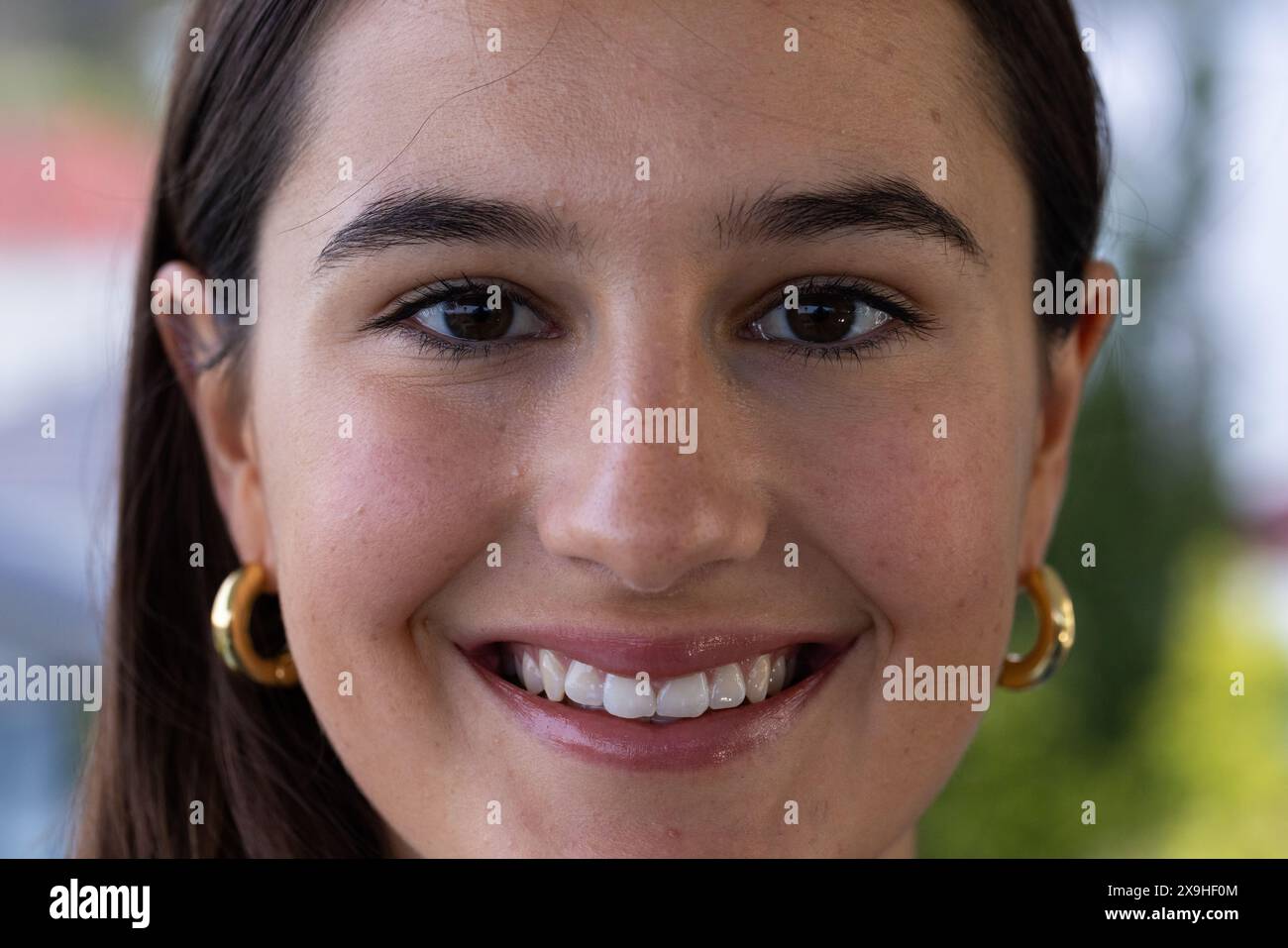 At home, young Caucasian woman smiling with gold hoop earrings. Enjoying a relaxing day at home spa with a serene outdoor view in background, feeling Stock Photo