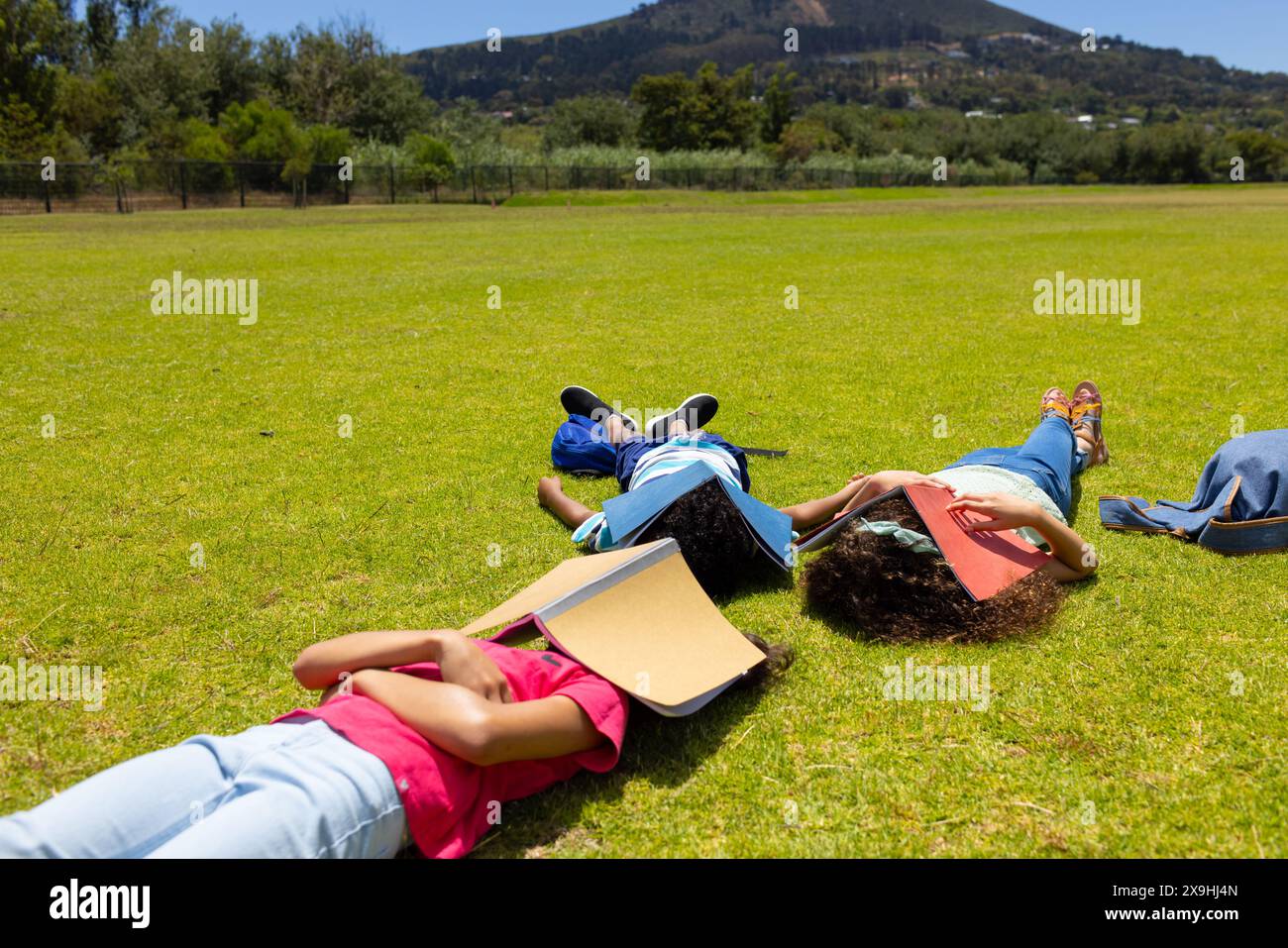 Three children are lying on the grass with books beside them, facing away from the camera Stock Photo