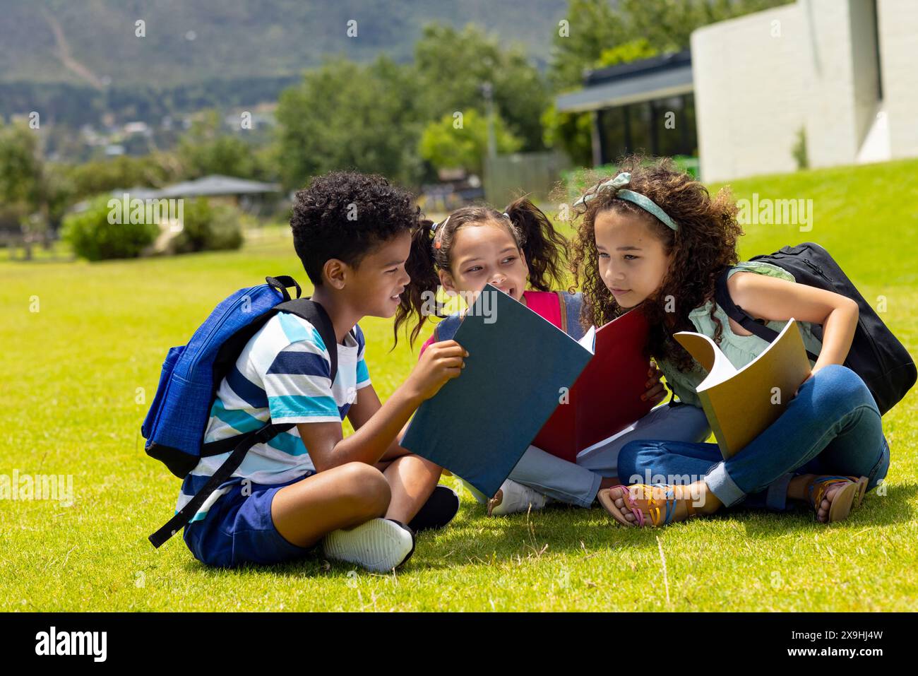 Biracial boy and two biracial girls are reading books outdoors Stock Photo