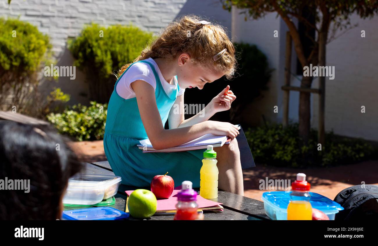 Caucasian girl with curly blonde hair is focused on reading outdoors in school Stock Photo