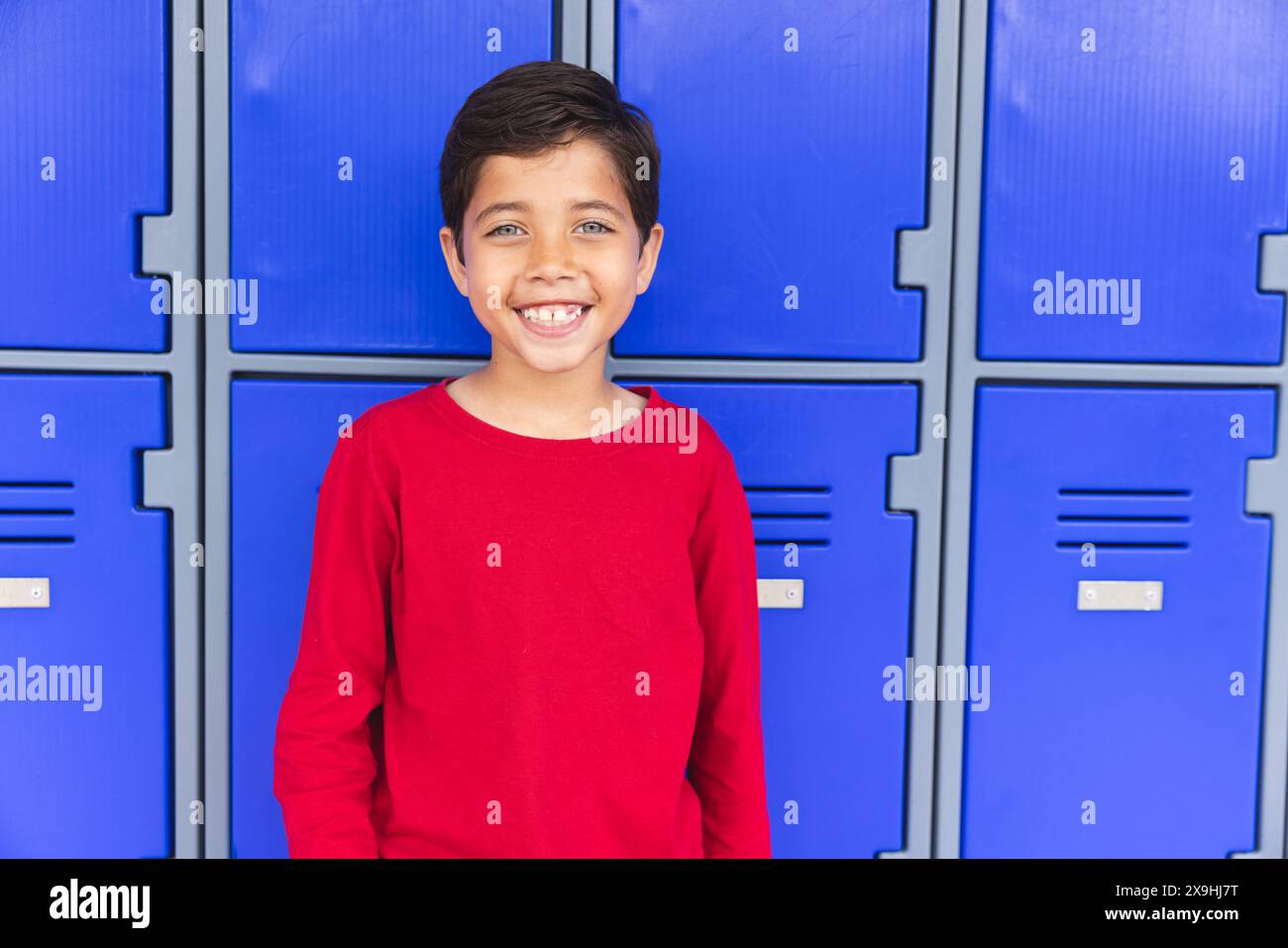 In school, young biracial male student standing in front of blue ...