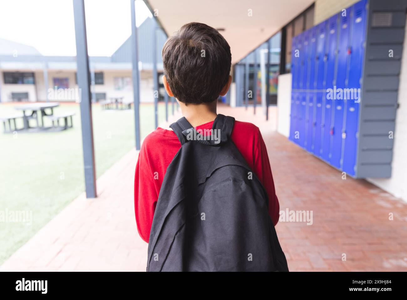 In school, biracial young boy wearing a red shirt and backpack walking ...