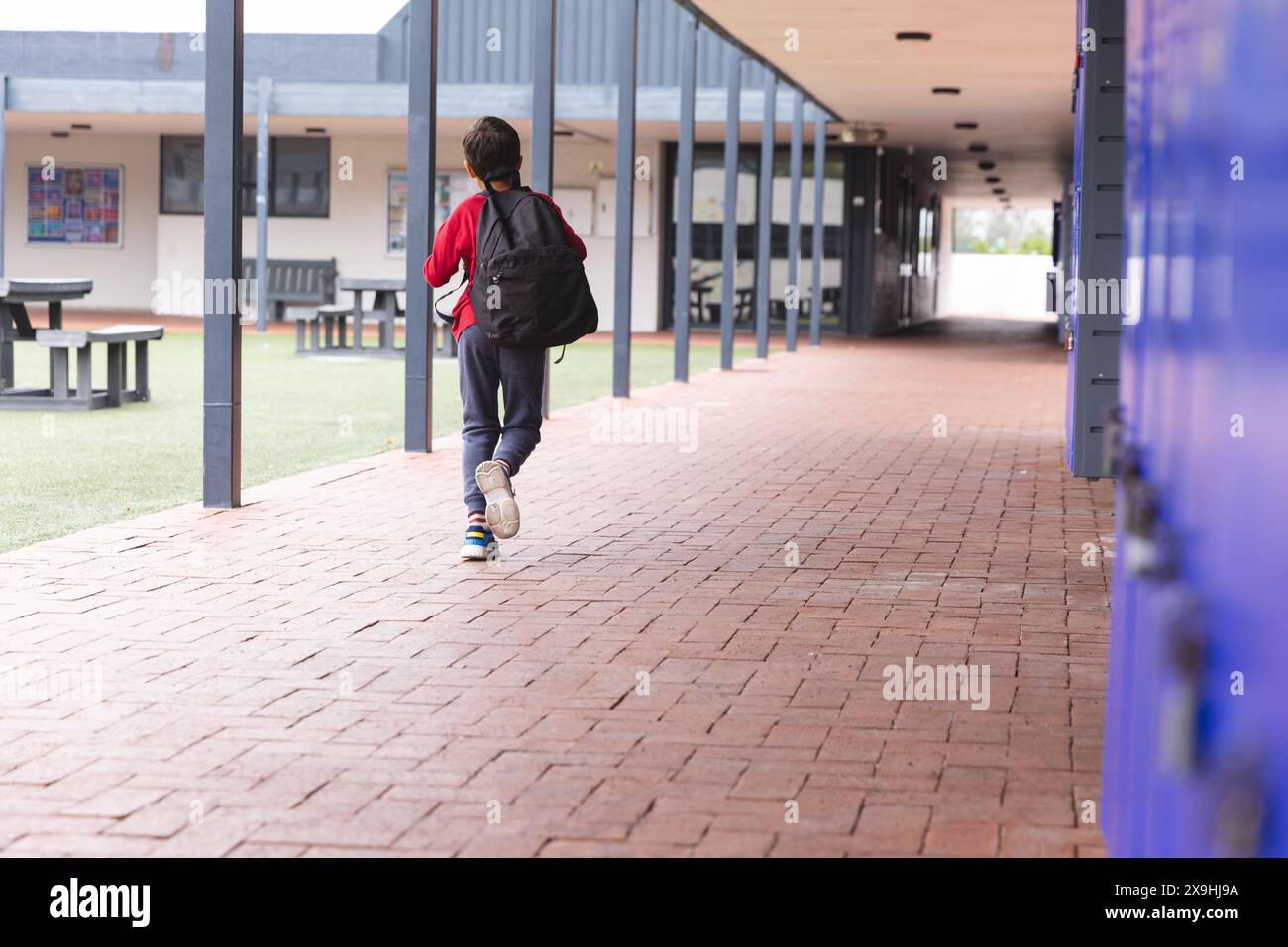 In school, young biracial male student walking alone outdoors with copy ...