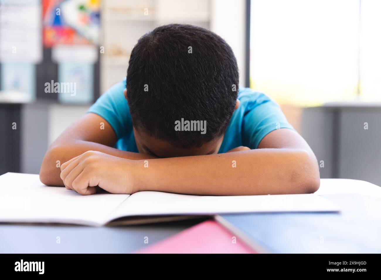 Biracial boy studying in a classroom, head resting on arms at school Stock Photo