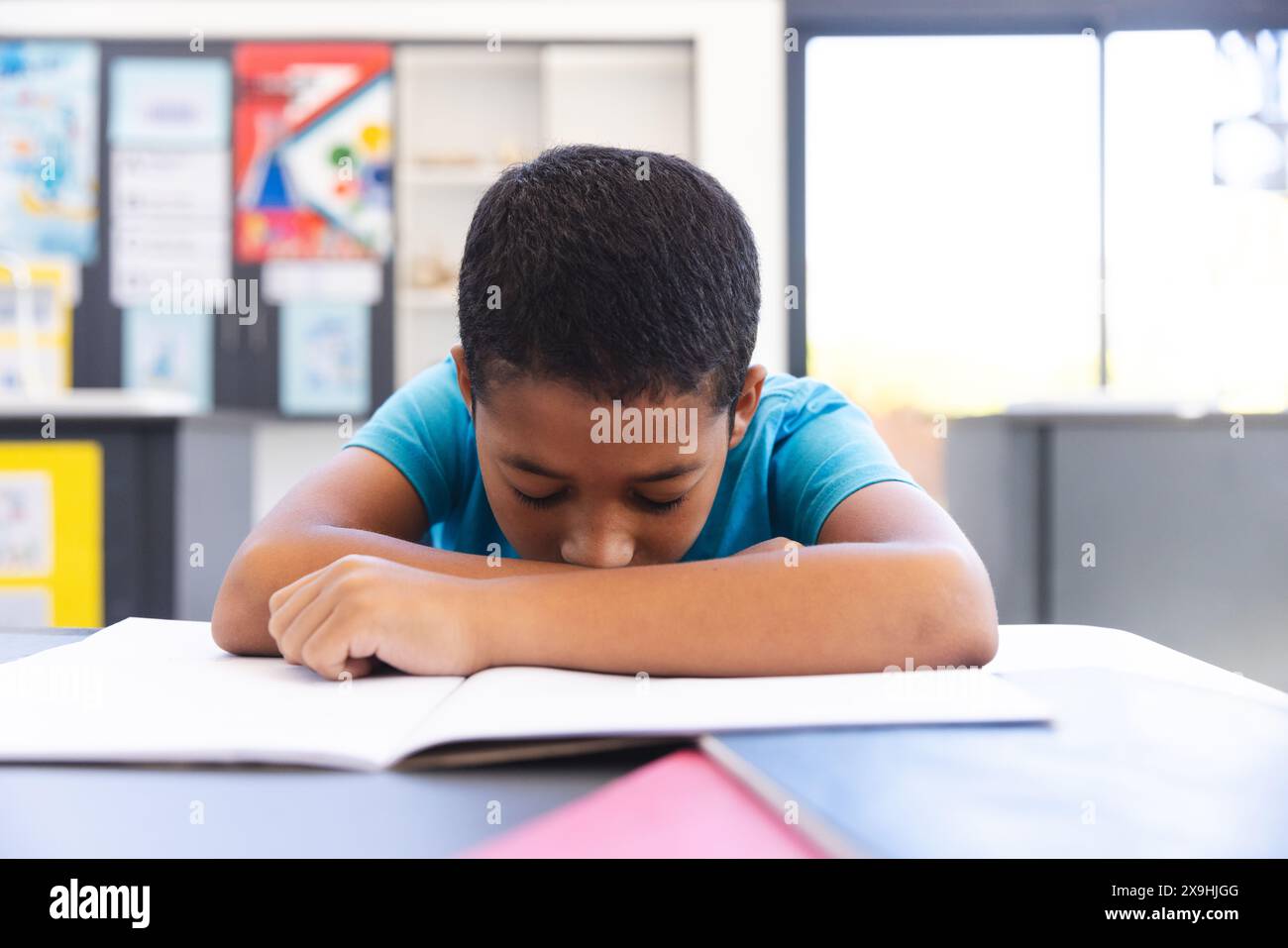 Biracial boy focused on reading a book in the classroom at school Stock Photo