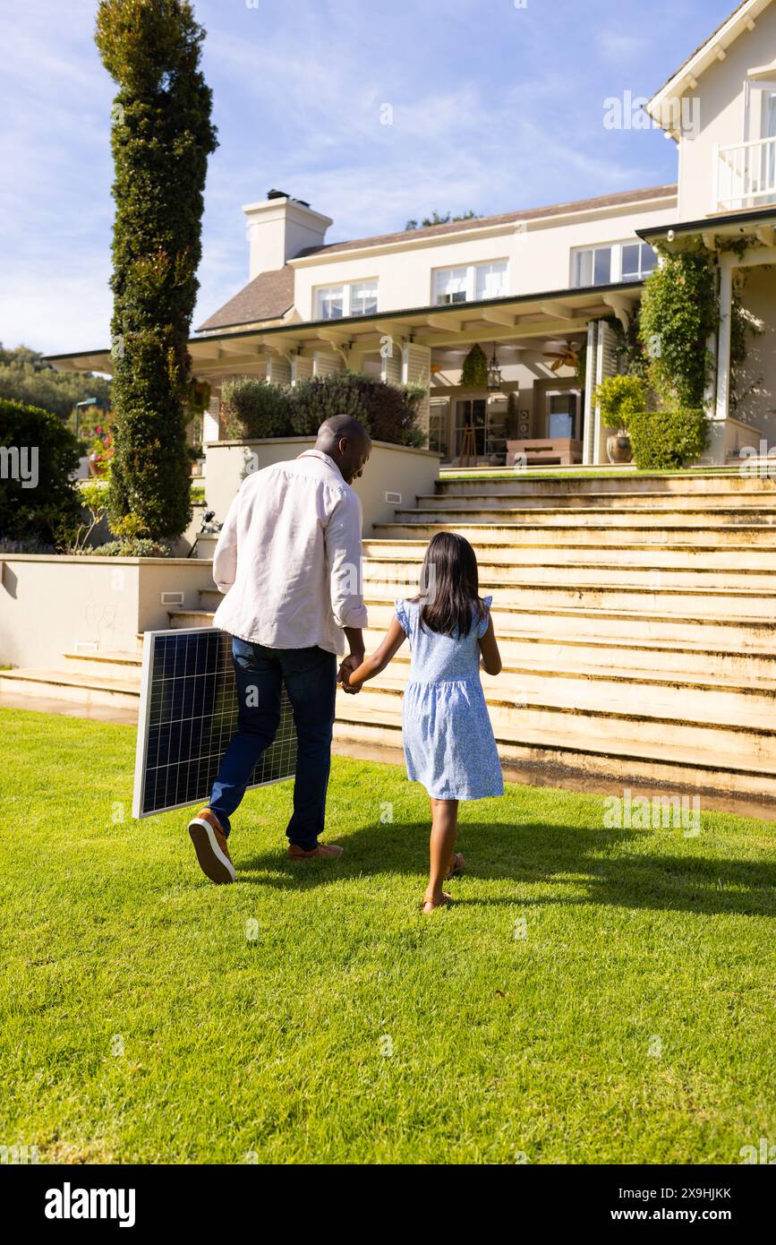 Outdoors, diverse father and daughter walking hand in hand with solar ...