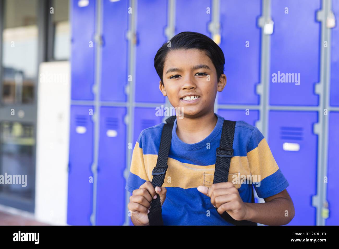 Biracial boy with a backpack stands in front of blue lockers in school ...