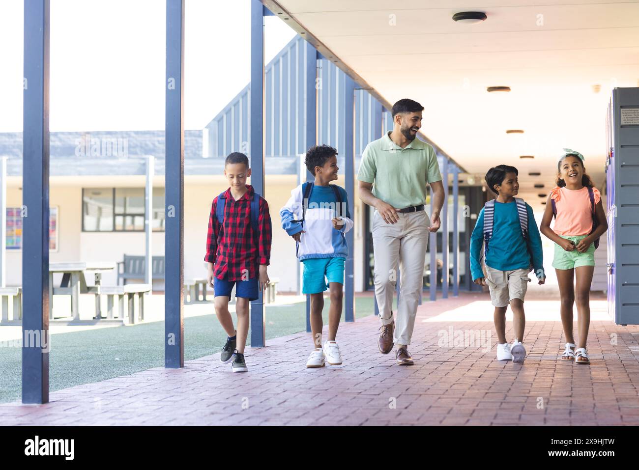 In school, diverse group of young students walking with their Asian teacher Stock Photo