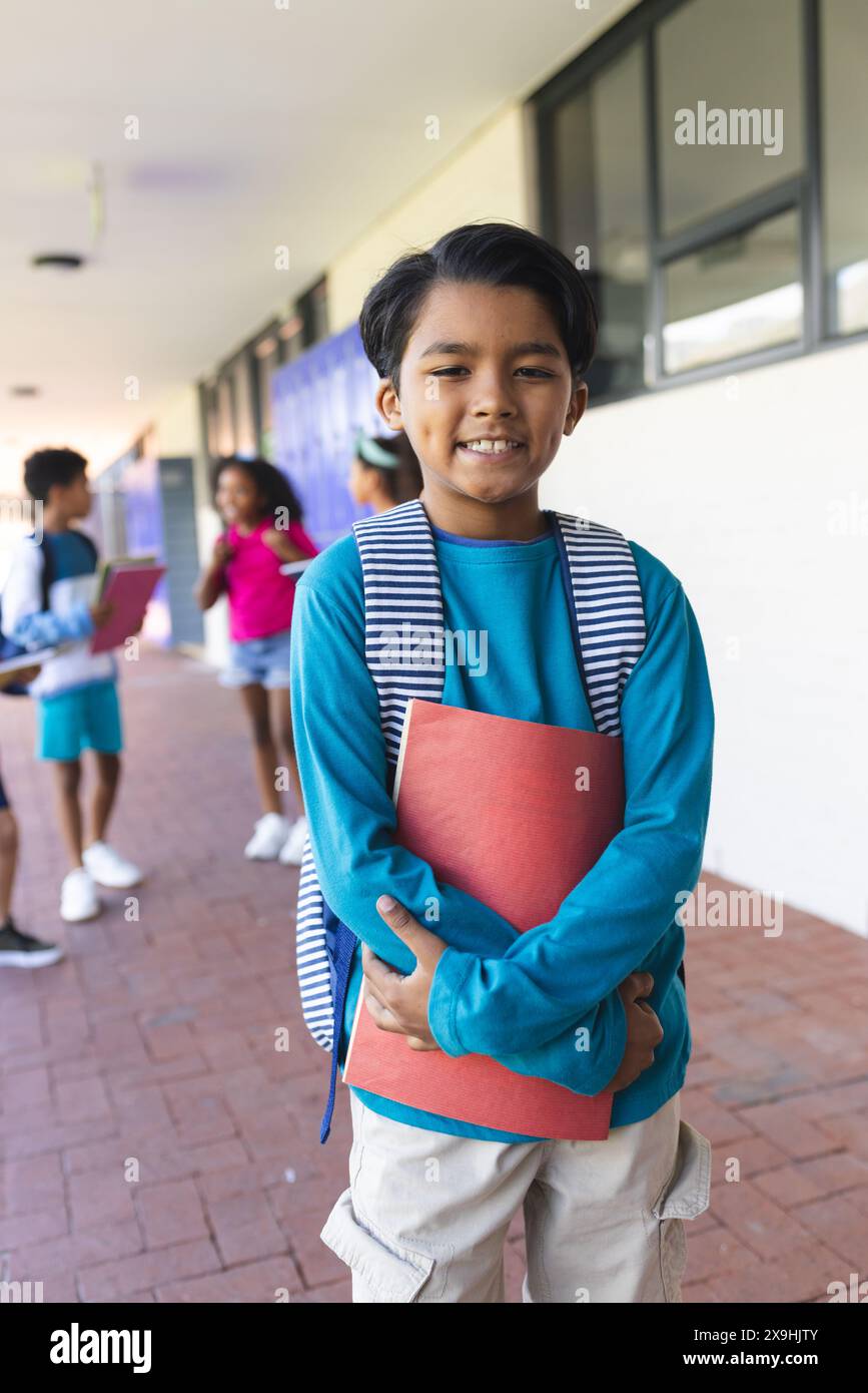 Biracial boy with black hair smiles, holding a red folder at school Stock Photo