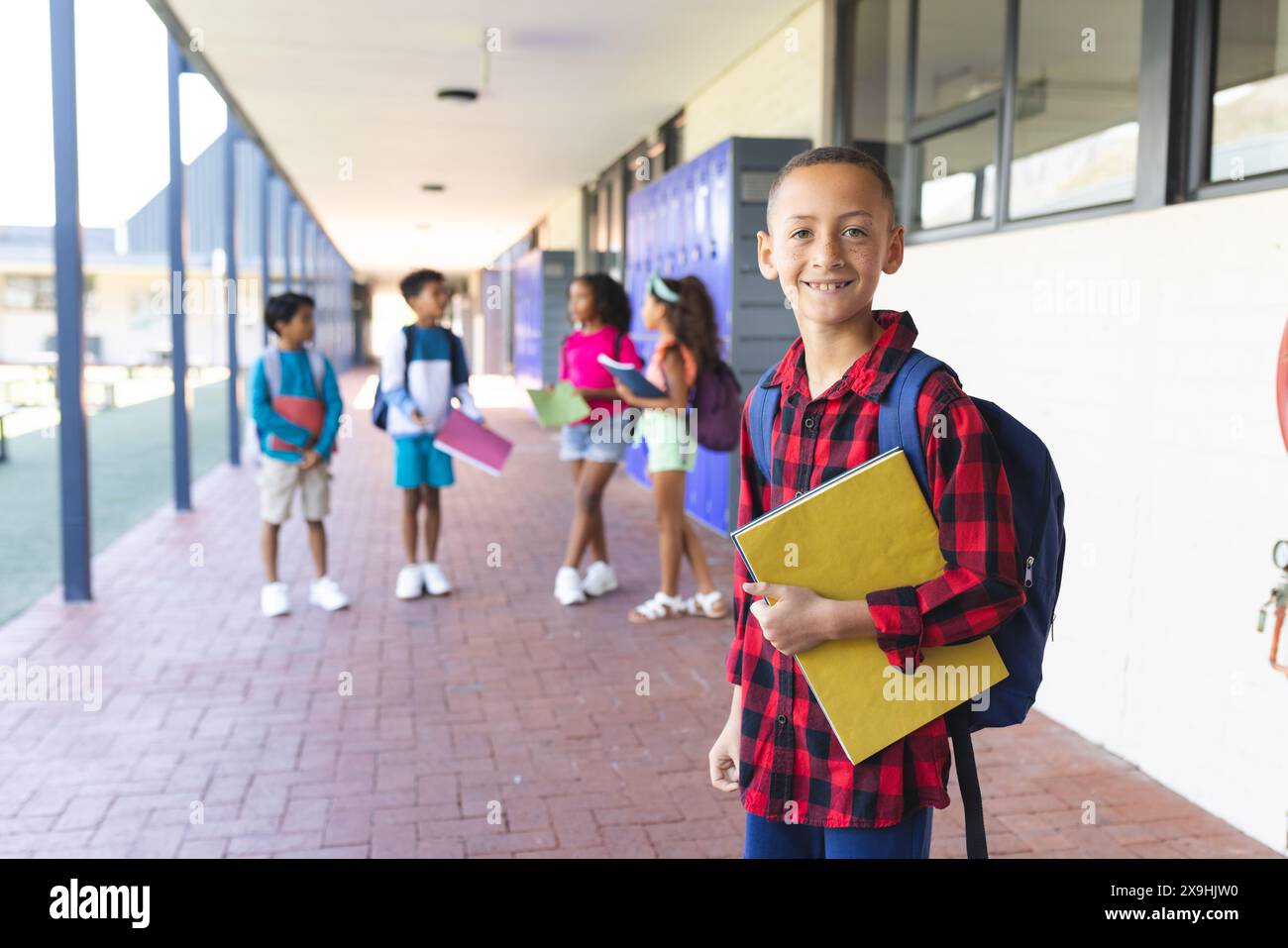Biracial boy with a red plaid shirt and backpack smiles in a school ...