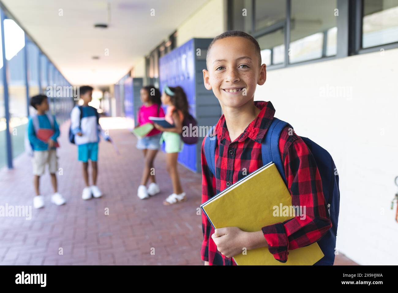 Biracial boy with a backpack stands smiling, holding a yellow folder in ...