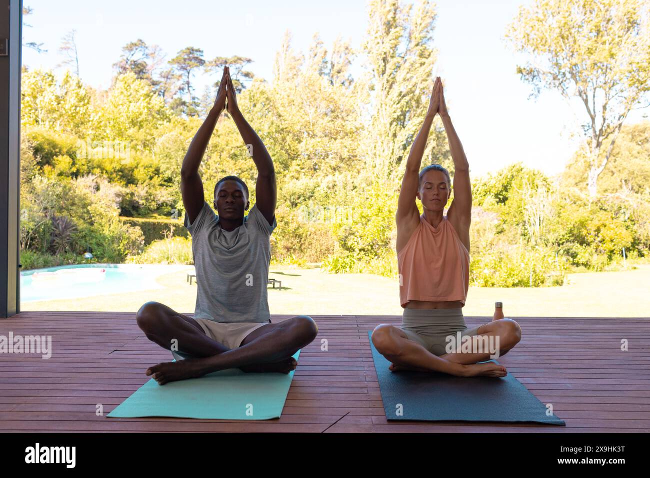 A diverse young couple practicing yoga outside beside pool Stock Photo