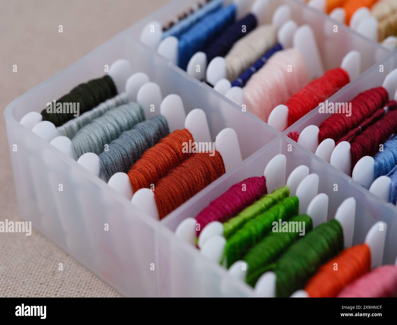 Plastic sorting box full of bobbins with different colour embroidery threads on a beige canvas background. Close-up Stock Photo