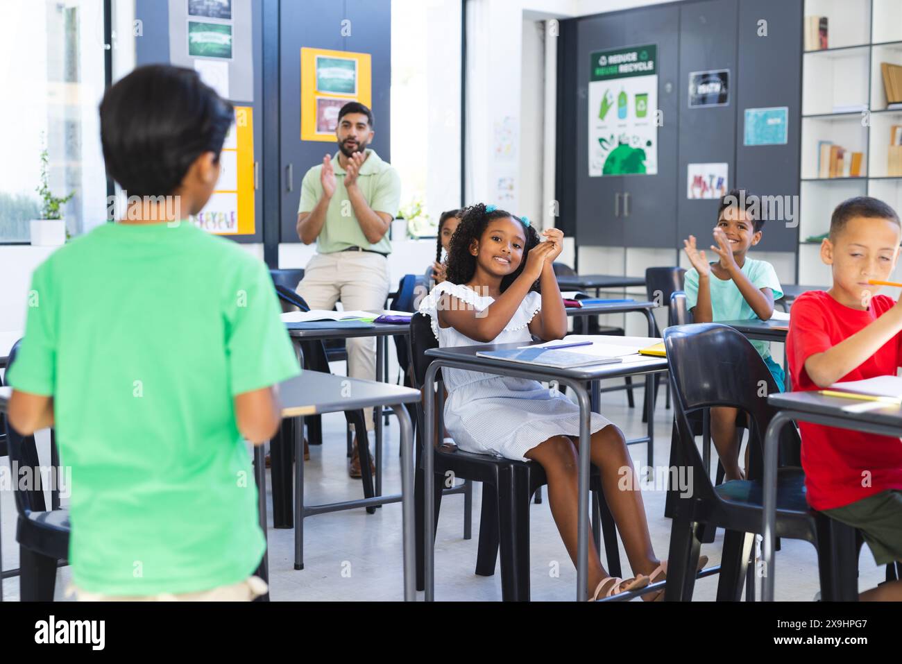 In school, Asian male teacher clapping hands while diverse students raising hands Stock Photo