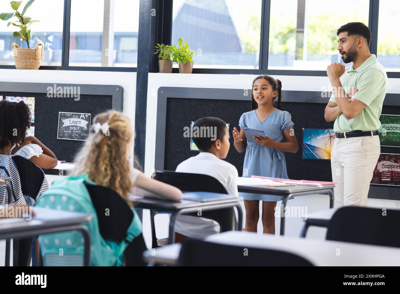 In school, young Asian male teacher listens to a biracial girl presenting Stock Photo