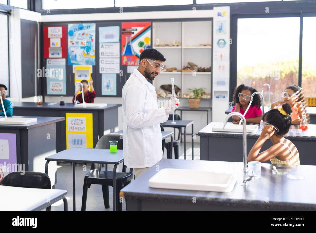 Asian male teacher with flask by diverse students in school science experiment Stock Photo
