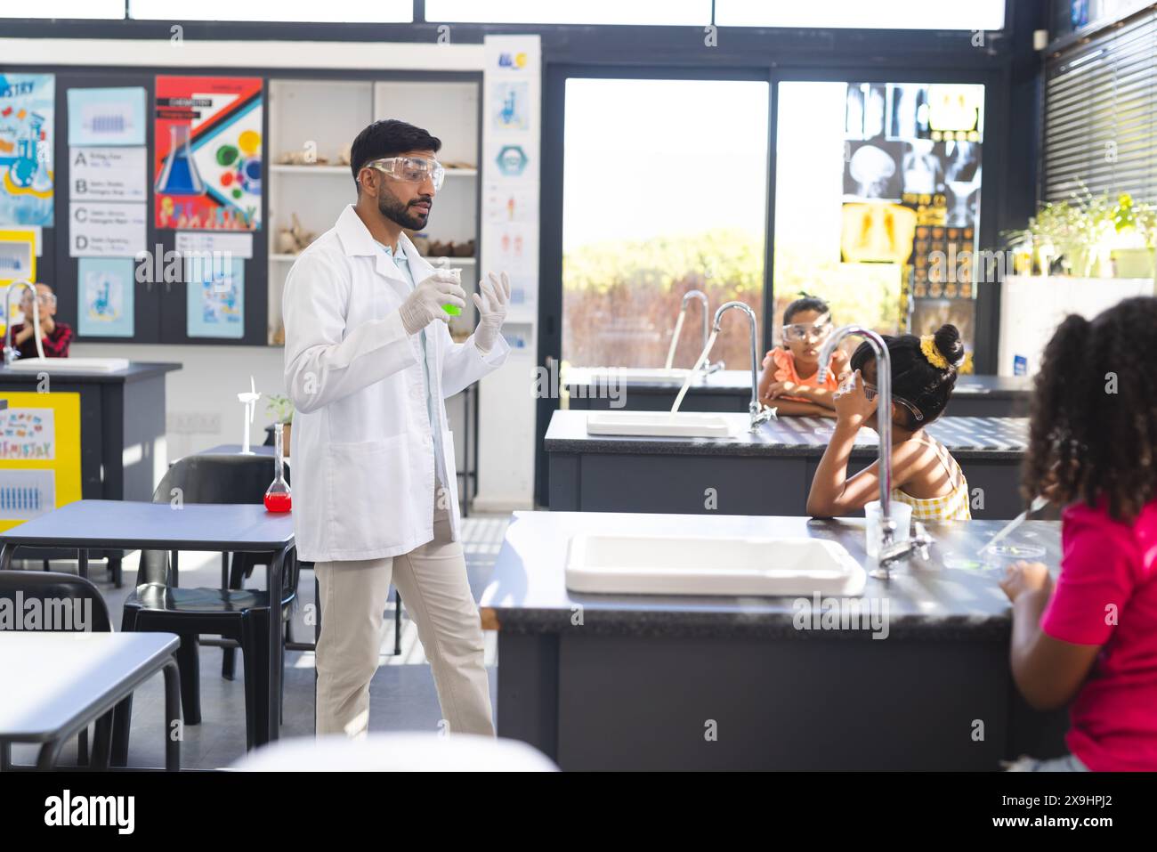 Young Asian male teacher in a lab coat conducts an experiment in school, holding a green liquid Stock Photo